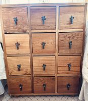 Front view of rustic wooden cabinet showing 12 drawers arranged in four rows and three columns with black iron hanging pull handles.
