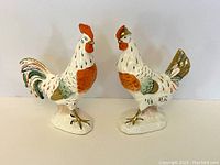 Front view of the pair of hand-painted rooster and hen figurines showing detailed coloration and gold accents on bases and feet.