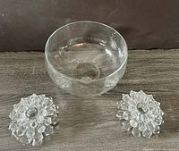 Pair of crystal candle holders and clear crystal bowl, all items shown from frontal view on wooden surface.