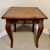 Front view of a wooden side table showing the square top, curved legs, and single drawer with a knob.