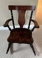 Front view of the dark stained oak rocking chair with visible contoured wood seat, turned arm supports, and incised backrest splat.