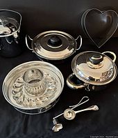 Overview photo showing the bundt pan, two saucepans with lids, a heart-shaped baking mold, melon scoop, candle snuffer, and a garlic press or similar small kitchen tool.