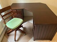Corner desk viewed from front showing drawers, beadboard sides, and pull-out trays, with swivel chair nearby.