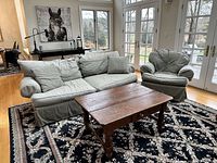 Full view of the gray upholstered down-filled sofa with two matching throw pillows and rustic mahogany coffee table on a patterned rug in a room with glass-paned double doors.