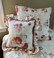 Close-up of two decorative throw pillows from Waverly Fashions, one with ruffles and both with red floral patterns on cream fabric.