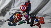 Full view showing assortment of superhero figures, motorcycles, small vehicles and toy skateboard