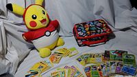 Full lot showing Pikachu plush doll, spread out Pokemon cards, and Pokemon lunch box.