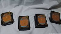 Four stacks of Magic The Gathering cards laid on a white sheet, showing card backs with classic design and color scheme.