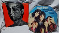 Photo showing front cover of both Rolling Stones albums, one 'Tattoo You' featuring tattooed face on red background and the other 'Through the Past, Darkly (Big Hits Vol. 2)' with band photo on blue background, worn edges visible.