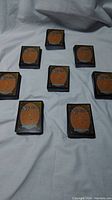 Eight decks of 50 Magic The Gathering cards laid out on a grey fabric surface, showing the card backs with the Magic The Gathering logo and circular design.