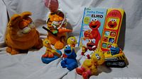 Photo showing all plush dolls, Sesame Street figurines, and Elmo Potty Time book with electronic toy device