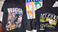 Three hip hop themed medium black T-shirts featuring Biggie, Selena, and Ice Cube, laid out flat.
