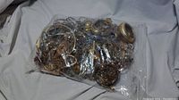 Large transparent bag full of mixed assorted jewelry items, tangled and layered, mostly gold and silver toned bracelets, earrings, pendants and more