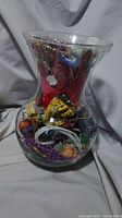 Large clear glass jar filled with various jewelry items seen from distance showing shape and volume
