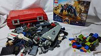 Overview of the lot with unopened Marvel Eternals box, red Lego carrier case, pile of loose Lego pieces, and a small built Lego vehicle.