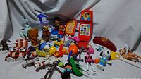 Full view of assorted toys including PlaySkool toy telephone, Groot figure, and multiple character toys scattered on a white background.
