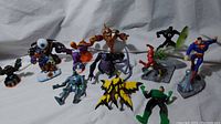 Wide shot showing 12 figures including Ben 10 Ultimate Alien, Haywire, DC Comics superheroes, and Skylanders characters on white backdrop.