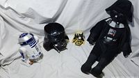 R2-D2 figure, Darth Vader black candy dish, gold mask, and plush doll displayed on white fabric background.