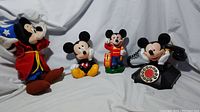 Photo showing the Sorcerer Mickey Mouse plush, seated Mickey Mouse bank, standing Mickey Mouse bank with drum, and vintage style rotary telephone Mickey Mouse.