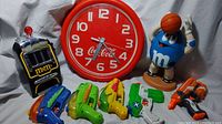 Photo showing the Coca-Cola clock, M&M slot machine dispenser, blue M&M character dispenser, and four Nerf squirt toys in multiple colors.