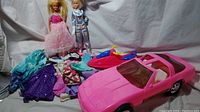 Photo of two Barbie dolls, one in pink dress and one in astronaut suit, pink Barbie Corvette toy car, jet ski toy and collection of doll clothes