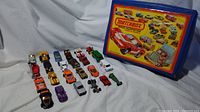 Photo of 20+ vintage 1970s die-cast cars arranged in rows with the blue Matchbox collector case showing the front graphic illustration of cars and text 'Matchbox Official Collector Case Holds 48 Models'.