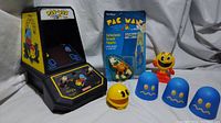 Full lot displayed including Coleco Pac-Man arcade game, carded bendy Pac-Man figure, plastic stand-up Pac-Man figure, wind-up rolling Pac-Man toy, and three blue ghost cups.
