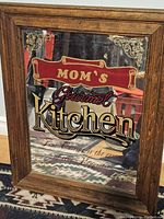 Mirror with wooden frame, ornate gold corner accents, and colorful slogan 'Mom's Gourmet Kitchen'