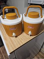 Two vintage orange Coleman coolers with white lids and large yellow caps, showing overall condition and model design