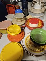 Photo showing assorted Tupperware containers, lids, plates with floral pattern, and some plastic mugs