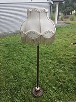 Full view of the vintage 1950s floor lamp with white fringe shade on grassy background