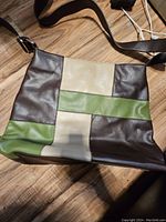 Front view of purse showing patchwork design of dark brown, cream, and avocado green sections on faux leather material.