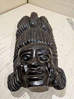 Front view of carved ebony mask showing facial details and vertical ridged hair design