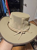 Full view of tan men's hat with mesh sides and braided band held in hand showing overall condition and shape