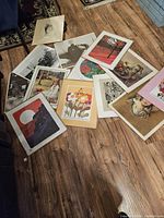 Multiple assorted art prints spread on floor showing variety of subjects including portraits, flowers, landscapes, and still life, each approximately 18x22 inches with white borders.