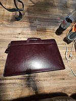 Full view of brown leather style briefcase on wooden floor, showing general condition and handle.