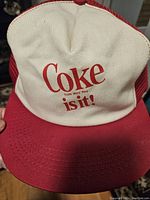 Front view of the vintage Coke 'Is it!' logo on white front panel with red brim.