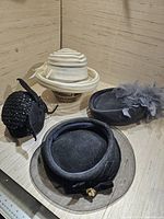 Four vintage fashion hats displayed on mannequin heads, showing various designs and materials.