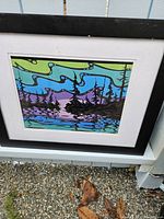 Photo of a professionally framed abstract water forest scene artwork in vibrant colors with black frame and white mat, placed outdoors to show the item clearly.