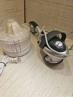 Photo showing electric citrus juicer and handheld massager placed next to each other on a wooden surface.