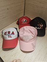 Four hats in the lot arranged on a wooden surface: USA Hockey, Canada Hockey, pink Dodge with ribbon, and black Rodeo with steer head
