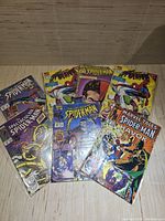 Seven Spider-Man comics laid out on a wooden surface, all individually bagged and appearing in very good condition with visible cover art showing titles such as The Spectacular Spider-Man and Marvel Tales Spider-Man.
