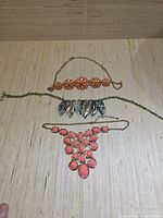 Three vintage costume jewelry necklaces laid side by side on a wooden surface, showing colors and designs distinctly.