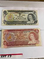 Photo showing both the Canadian 1 dollar and 2 dollar bills with visible front sides; details such as serial numbers and portraits visible.