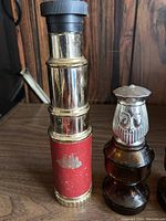 Photo of tall brass/red telescope-shaped Avon bottle with ship emblem and owl-shaped brown glass bottles present.
