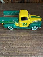 Left side view of vintage Beaver Lumber Ford truck with green flatbed and yellow-green cab on wood surface.