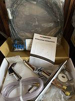 Unboxed view showing chrome kitchen faucet parts, flexible braided hose coiled in original plastic packaging, and installation instructions.