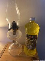 The lantern and the full bottle of lamp oil sitting side by side on a wooden surface.