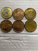 Top view of 6 Canadian one dollar coins, one colored uncirculated coin at top-left, others various circulated Loonie designs, some commemorative.