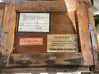 Top view of the wooden crate showing metal latches and various original labels including shipping and contract information from Canadian Aviation Electronics Ltd.